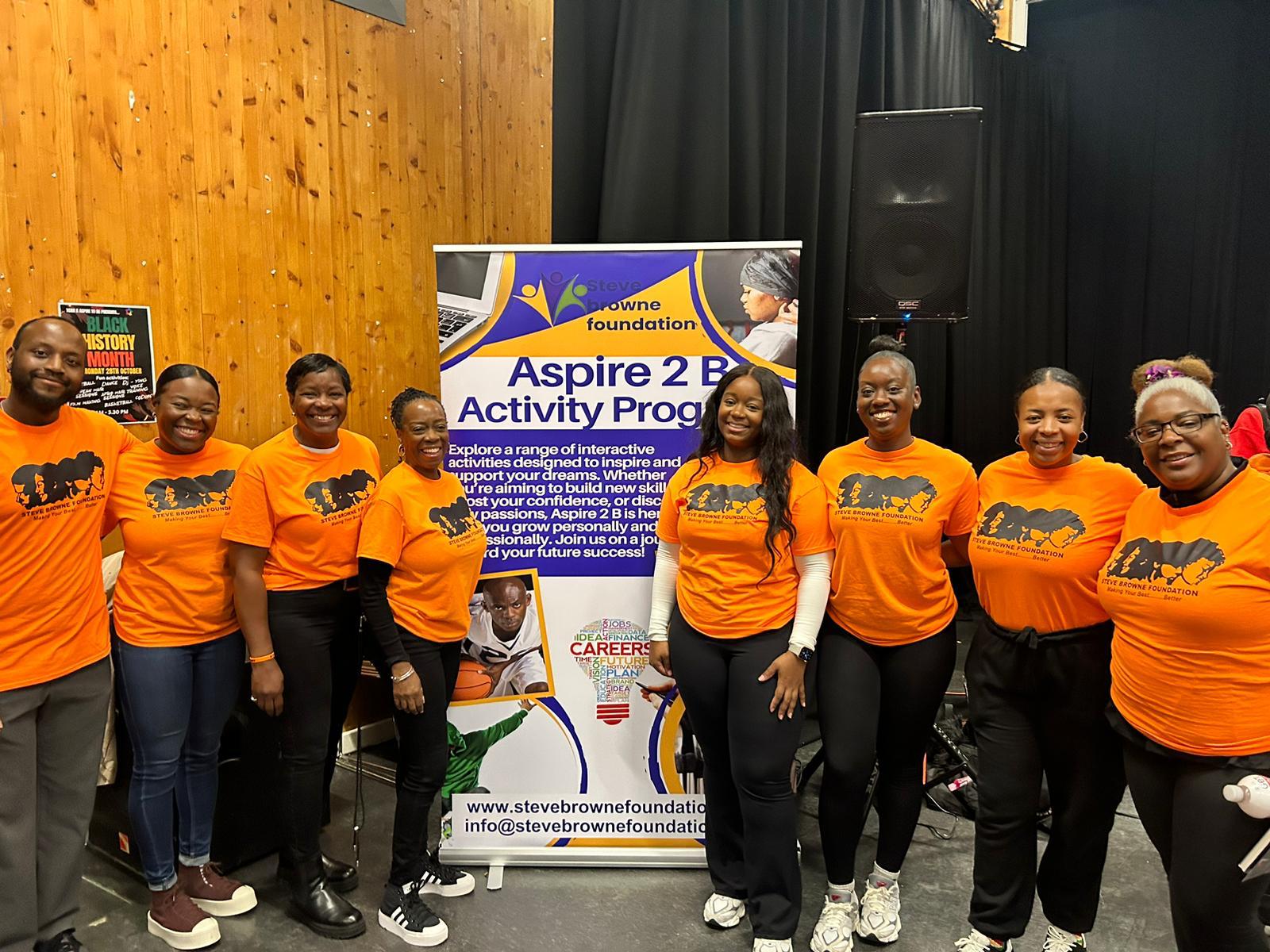Aspire 2 B team in front of the programme banner
